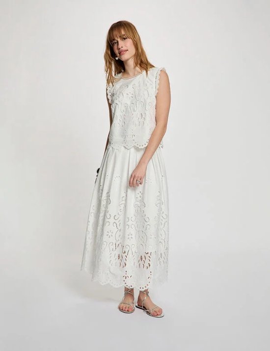 Model in een witte kanten top met kanten mouwtjes en een witte kanten maxirok.