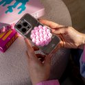 Roze telefoonsticker met zuignapjes op een telefoonhoesje, getoond in handen met een spiegelend oppervlak.