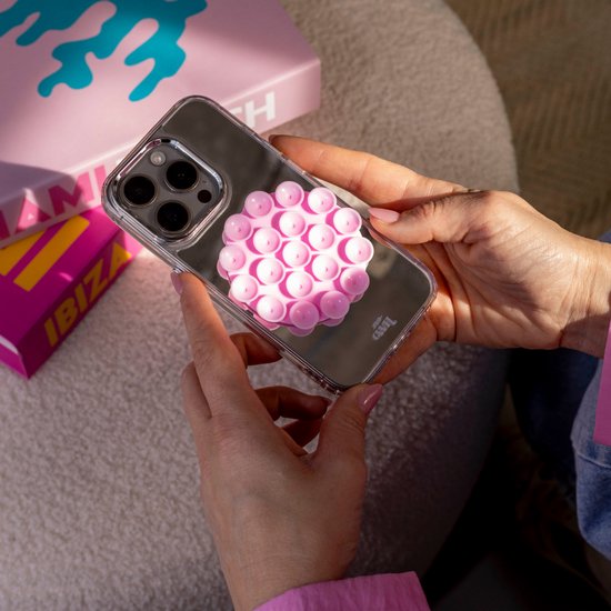 Roze telefoonsticker met zuignapjes op een telefoonhoesje, getoond in handen met een spiegelend oppervlak.
