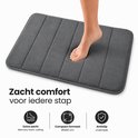 Tapis de bain gris côtelé, avec un pied qui monte dessus. Le tapis a un rembourrage en mousse à mémoire de forme.