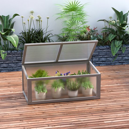 Grijze houten mini-kas met deksel open, gevuld met planten in potten, op een houten terras.