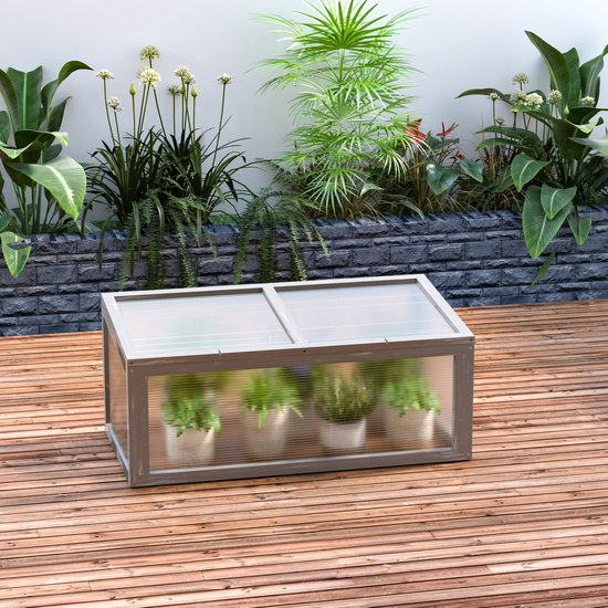 Grijze houten mini-kas met transparante deksel en zijden, gevuld met planten, op een houten terras.