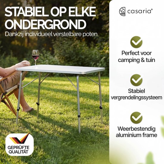 Zilverkleurige campingtafel met wit tafelblad op individueel verstelbare poten in gras.