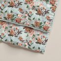 Een detail van een lichtgroen dekbed met een print van roze en oranje bloemen en groene bladeren.