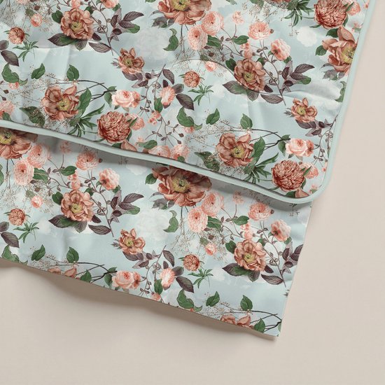 Een detail van een lichtgroen dekbed met een print van roze en oranje bloemen en groene bladeren.