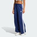 Model in een donkerblauwe wijde trainingsbroek met witte strepen op de zijkanten en witte sneakers.