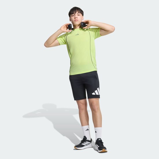 Jongen met koptelefoon, draagt geel T-shirt met korte mouwen en zwarte shorts met Adidas logo.