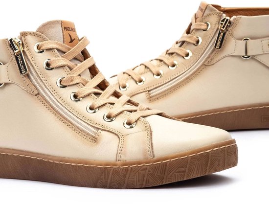 Close-up van crèmekleurige leren hoge sneakers met ritssluiting, gespdetail en veter.
