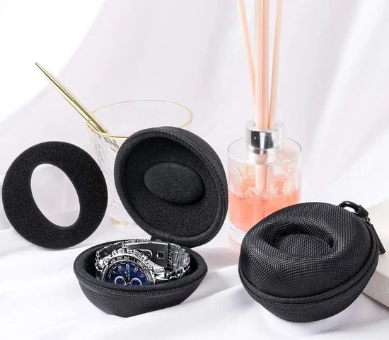 Blauw horloge met zilverkleurige band in een open zwart etui. Naast het etui liggen een zwarte ring, een glazen potje en een diffuser.