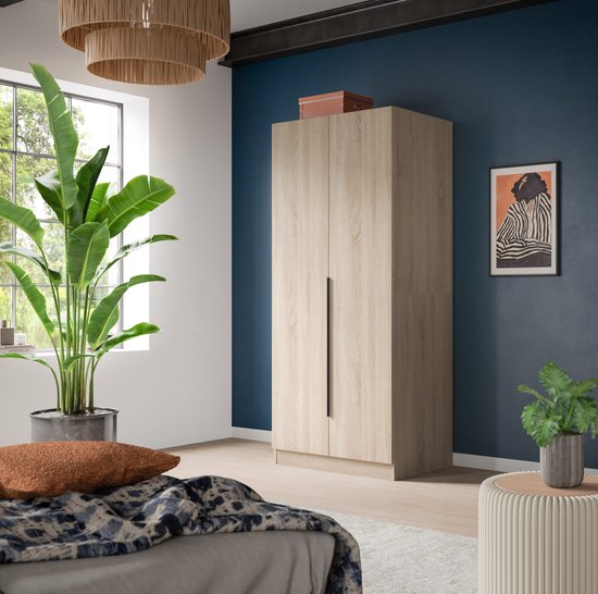 Houten kledingkast met twee deuren en zwarte handgrepen, in een slaapkamer.