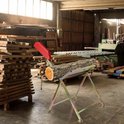 Houten boomstam op een metalen zaagbok met rode kettingzaaghouder in een werkplaats.