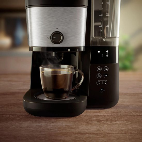 Een glas stomende koffie staat onder een Philips koffiezetapparaat, met digitaal display.