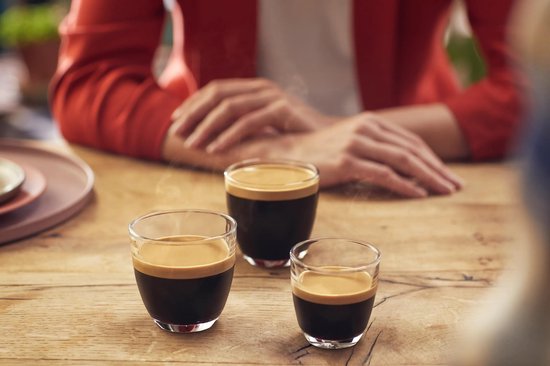 Drie kopjes espresso met schuim op een houten tafel.