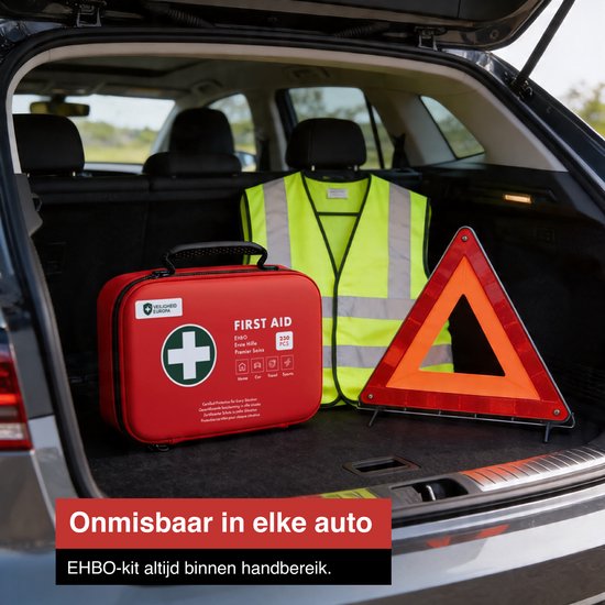 Rode EHBO-koffer met veiligheidshesje en gevarendriehoek in de kofferbak van een auto.