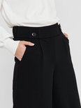 Close-up van de tailleband van een zwarte wijde broek met twee knopen en steekzakken.