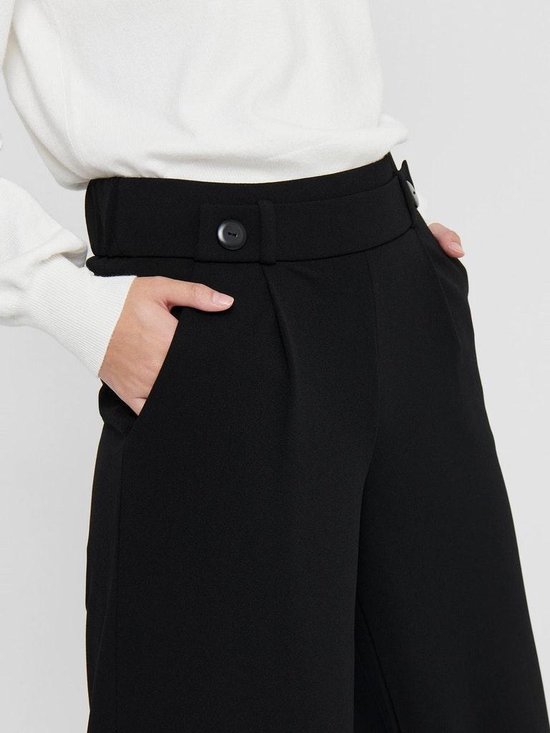 Close-up van de tailleband van een zwarte wijde broek met twee knopen en steekzakken.