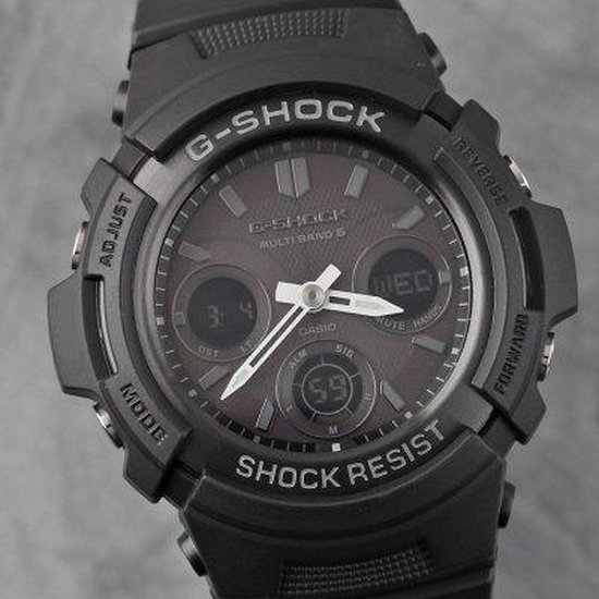 Gedetailleerde weergave van een zwart G-Shock horloge met donkergrijs display, analoge wijzers en digitale sub-dials. 'SHOCK RESIST' is zichtbaar.