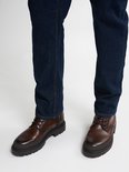 Model draagt donkerblauwe jeans en bruine veterschoenen.