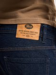 Bruin leren merklabel op de achterkant van een donkerblauwe jeans met de tekst 'Petrol Industries Denim Driven Since 1989'.