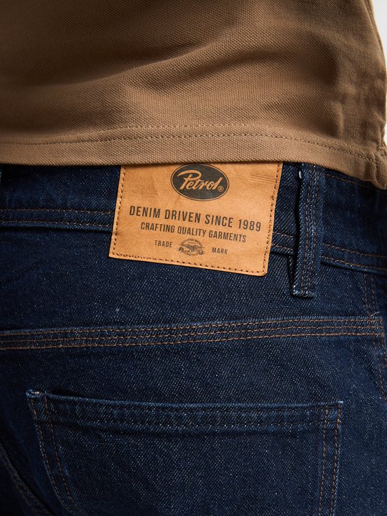Bruin leren merklabel op de achterkant van een donkerblauwe jeans met de tekst 'Petrol Industries Denim Driven Since 1989'.