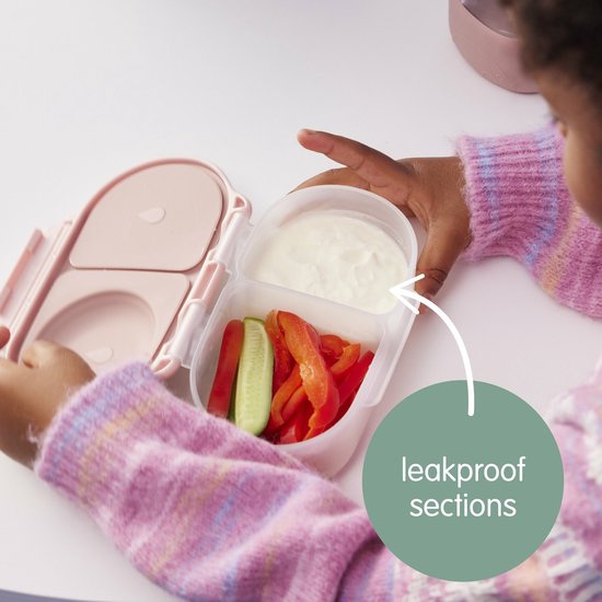 Mains d'enfant remplissant les compartiments étanches d'une boîte à goûter b.box rose pâle avec des légumes et une sauce.