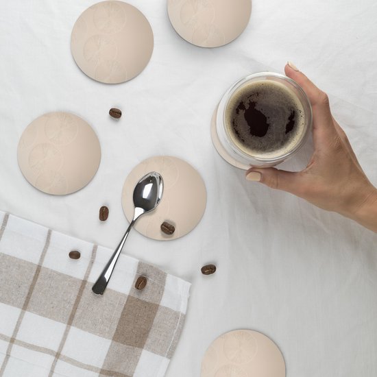 Une main tient un verre de café au-dessus d'un sous-verre rond beige à motif de cercles.