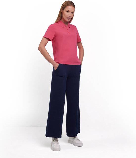 Model met lange blonde haren draagt een koraalroze Falke poloshirt en marineblauwe broek.