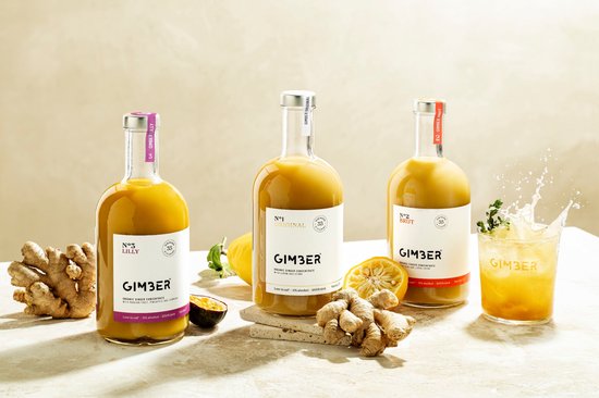 Drie flessen Gimber: Lilly, Original en Brut. Naast staan citroen, passievrucht, gember en een glas met spattend drankje.
