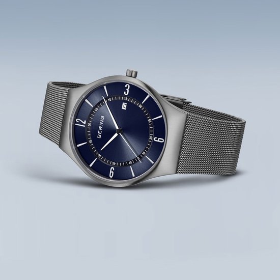 Grijs BERING horloge met blauwe wijzerplaat en mesh band, schuin van voren gezien.