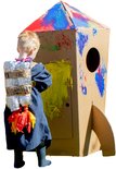 Jongetje met zelfgemaakte rugzak schildert op een kartonnen raket. De raket is versierd met primaire kleuren.