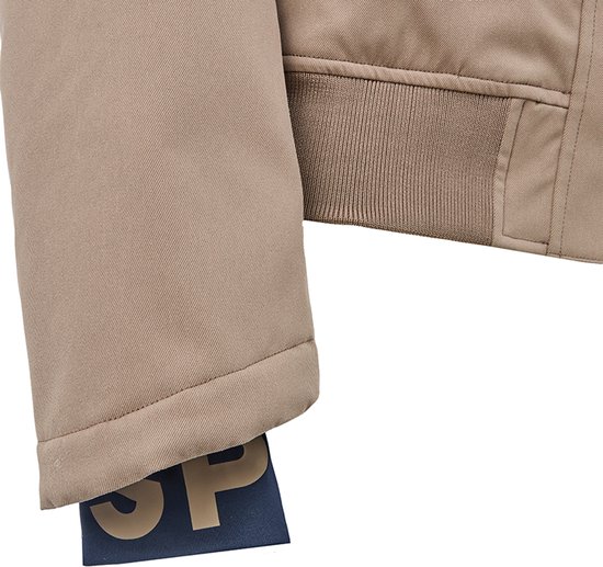 Détail de veste beige pour femme avec ourlet côtelé et étiquette bleu marine avec 'SP'.