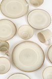 Verschillende beige borden, mokken en kommen met een bruine rand, gerangschikt op een witte achtergrond.
