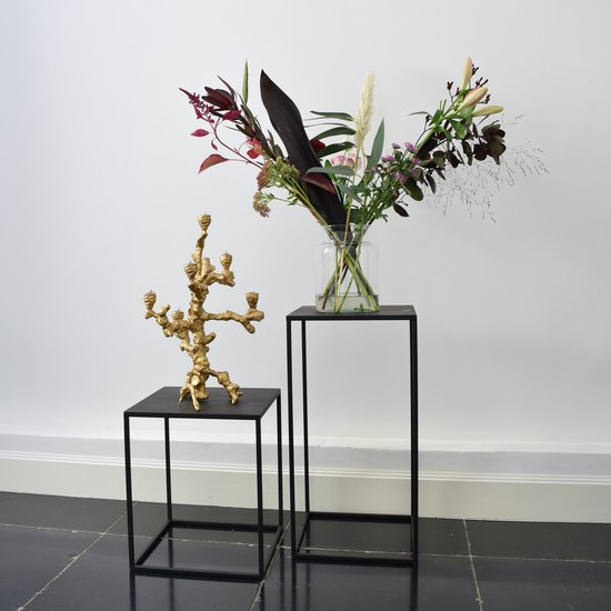 Twee zwarte metalen zuilen, één met een gouden kandelaar en één met een boeket bloemen.