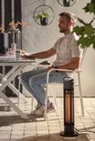 Een man zit aan een tuintafel met een zwarte staande infrarood heater ernaast.