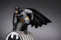 Gedetailleerde Batman-figuur in grijze outfit, hurkend boven een lichtgevende schijnwerper.