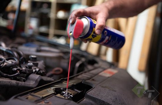 Hand spuit WD-40 met rode sproeibuis in een motorruimte van een auto.