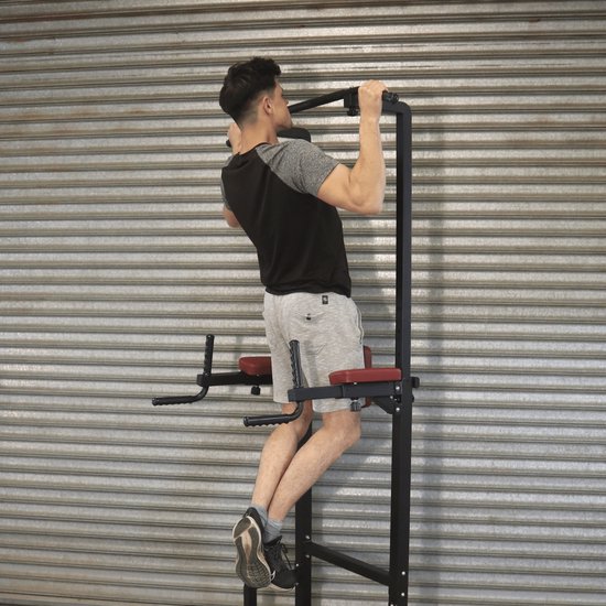 Man trekt zich op aan de zwarte pull-up bar van een krachtstation met rode kussens.