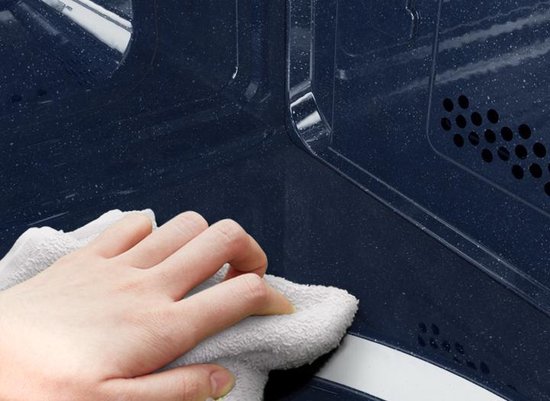 Hand veegt blauw interieur van magnetron schoon met witte doek.