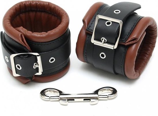 Zwart leren enkelboeien met bruine voering en gespen, met metalen ketting en karabijnsluitingen.