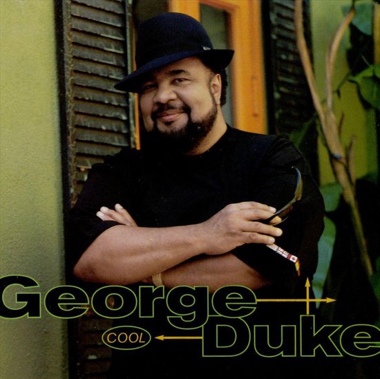 George Duke in zwart shirt, zwarte hoed en zonnebril in hand.