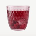 Verre rose avec une boisson rouge, des framboises et des glaçons. Le verre a un motif en relief de formes ovales.