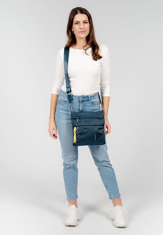Model met donkergroene schoudertas, jeans en witte trui.