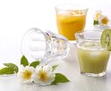 Duralex Picardie glazen met drankjes. Eén glas met groene drank en kiwi, één met oranje drank en oranjeplakjes. Twee witte bloemen.