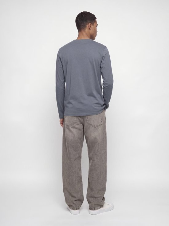 Een model van achteren gezien, draagt een grijs shirt met lange mouwen en een bruingrijze jeans.