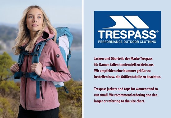 Vrouw met roze Trespass outdoorjas met capuchon, blauwe rugzak en bergen op de achtergrond.