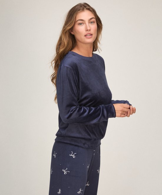 Model in een donkerblauwe velours pyjamaset, met strikje print op de broek.