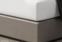 Une base de lit grise avec un drap-housse blanc par-dessus.