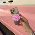 Roze ronde zuignapsticker op een glinsterende transparante iPhone-hoes, vastgehouden tegen een roze voertuig.
