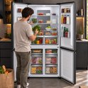 Man plaatst verse groenten in een open, donkergrijze Heinner Amerikaanse koelkast in een moderne keuken.