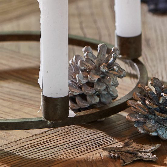 Close-up van roestbruine kaarsenkrans met brandende witte kaars en dennenappels op een houten ondergrond.